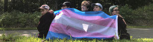5 campers pose and look over from behind the transgender pride flag